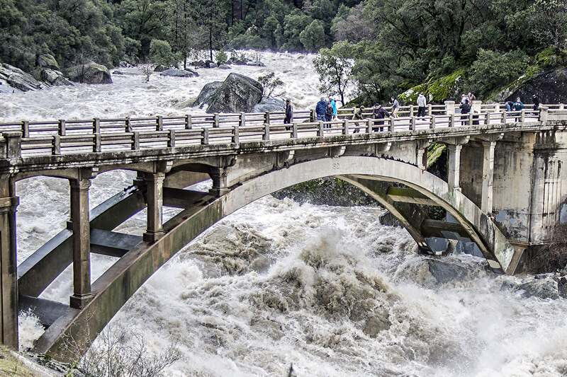 Muddy brown floodwater rushing under the old Highway 49 arch bridge on the South Yuba River.